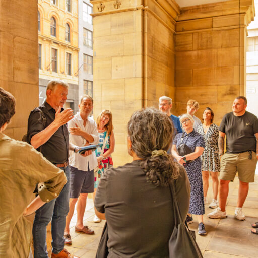 Tour group gathered under a stone archway as Jonathan Schofield leads a walking tour, sharing stories about the city.