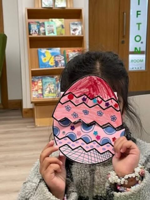 Child holding a coloured-in Easter egg in front of their face